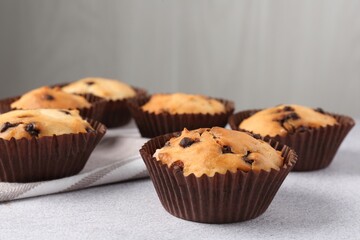Delicious muffin with chocolate chips on light grey table, closeup