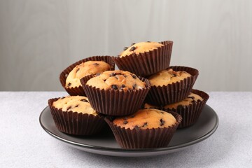 Delicious muffin with chocolate chips on light grey table, closeup