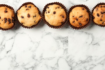 Delicious muffin with chocolate chips on white marble table, flat lay. Space for text