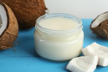 Coconuts and cooking oil on light blue wooden table against white background