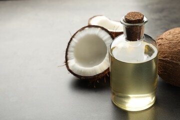 Organic coconut cooking oil in glass bottle and fresh fruits on grey table, closeup. Space for text