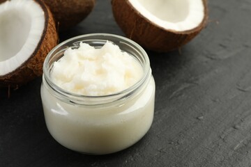 Organic coconut cooking oil in glass jar and fresh fruits on black table, closeup. Space for text