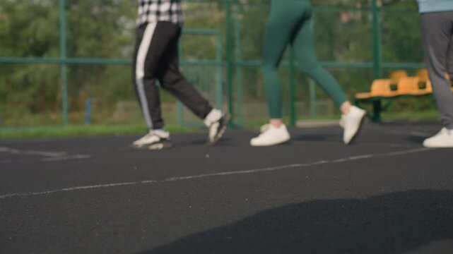 Three leg view of two women jogging, one in green joggers and another in ash joggers with white sneakers, with a blurred background of a bar fence and people seated outdoors