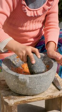 vertical latina girl hands chopping tomato in mortar or also called batan in the backyard of her house in la paz - cooking concept