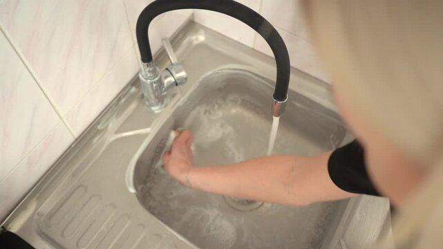 Cleaning kitchen sink of stainless steel with foamed detergent product and brawn sponge. Scrubbing the dirt. Slow motion.