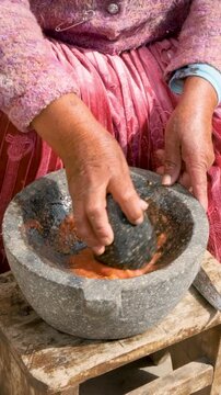 vertical hands of old woman of the aymara chola culture grinding in a mortar or also called batan in the courtyard of her house in la paz, bolivia - cooking concept