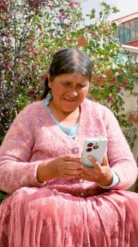 vertical Cholita adult woman in pollera holding her cell phone in the courtyard of her home in La Paz, Bolivia - concept of older adults