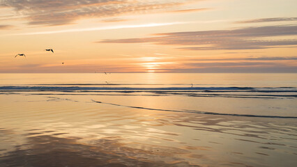 Describe a serene sunrise over the calm, glassy waters of a secluded beach. 