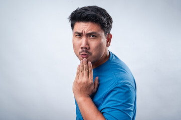 An Asian man wearing a blue t-shirt against a white isolated background is expressing surprise or shock. His mouth is slightly open, and his hand covers it in a playful or astonished manner.