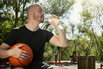 Athletes handsome man drinking water after active workout on outdoor sports ground. Water balance...