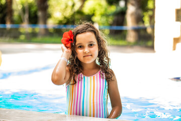 Naklejka premium Happy kid little girl playing in outdoor swimming pool at sunny day. Active vacation and healthy lifestyle. Happy summertime.