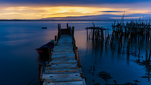 An old wooden fishing pier in Portugal in the area of Setubal at sunrise and low tide. Carrasqueira palafitic pier. A dilapidated fishing pier. Torso of a fishing pier.  - Powered by Adobe