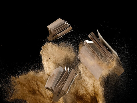 Flying books in dry sand explosion on black background, studio shot