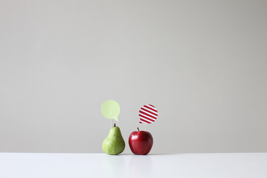 Red apple and green pear side by side on a table with speech bubbles