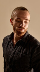 Fototapeta premium Portrait of handsome bearded man with tied up hair, in black shirt design with confidence against warm toned background. Concept of male beauty, skin care, fashion, wellness