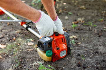 Starting a gas mower to cut grass. A man pulls the recoil starter to start the engine