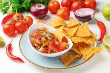 Delicious salsa (Pico de gallo) served with nachos and ingredients on white wooden table, closeup