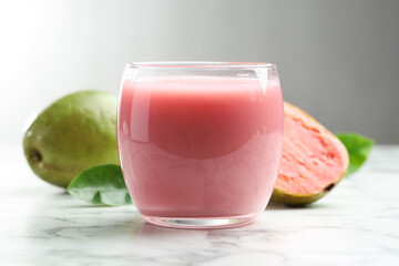 Tasty guava juice in glass, leaves and fruits on white marble table against grey background, closeup