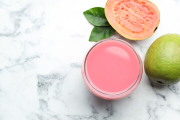 Tasty guava juice in glass, leaves and fruits on white marble table, flat lay. Space for text