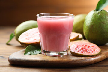 Tasty guava juice in glass, leaves and fruits on wooden table, closeup