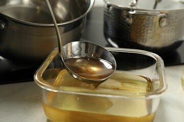 Pouring used cooking oil into glass container at white countertop, closeup