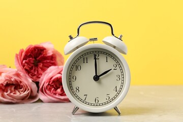 Spring time. Alarm clock and beautiful roses on grey marble table against yellow background