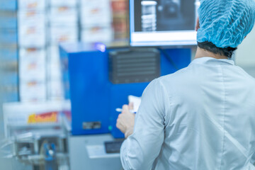 A factory worker inspects product packaging with a computerized scanning system. This image highlights industrial automation, food safety, quality assurance, and manufacturing standards.
