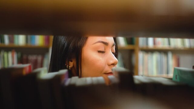 Close-up of a young woman scanning books on a shelf in a quiet bookstore. Thoughtful female reader browsing through titles in a cozy library, focused on finding her next book.