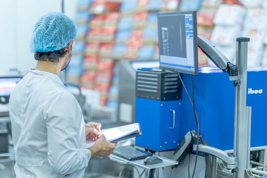 A factory worker inspects product packaging with a computerized scanning system. This image highlights industrial automation, food safety, quality assurance, and manufacturing standards.