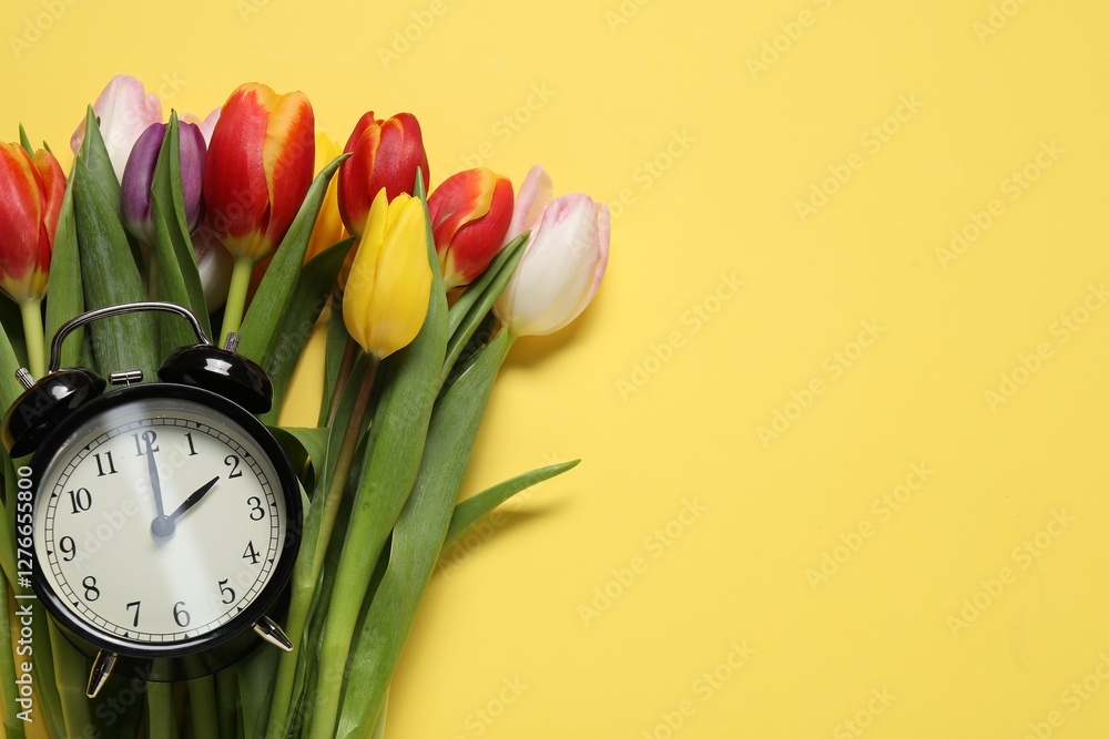 Poster spring time. alarm clock and beautiful tulips on yellow background, flat lay. space for text