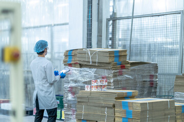A quality control worker in a sterile manufacturing facility inspects cardboard packaging. Wearing...