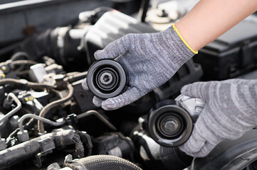 Auto mechanic in gloves repair car, and holds belt pulley and serpentine belt tensione in his hands...
