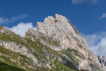 A close view of the iconic Seceda ridge in South Tyrol, Italy, highlighting the striking contrasts between rocky cliffs, grassy patches, and the deep blue sky on a sunny summer day
