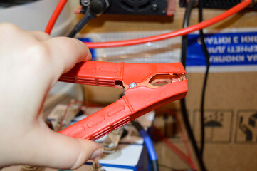 Obraz premium hand holding red jumper cable clamp battery system connected wiring setting technical electrical environment energy storage automotive repair off-grid power solutions charging upkeep renewable energy 