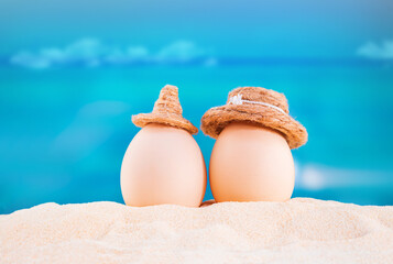 Happy easter. White eggs with hats on sandy beach of sea or ocean. Holiday postcard in hot country. Travel, spring, summer, vacations. Copy space