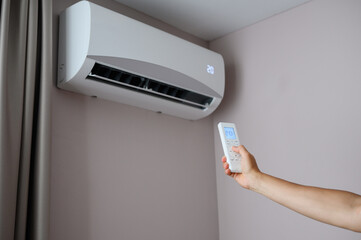 Woman holding air conditioner remote control with display showing 20 degrees Celsius temperature in...
