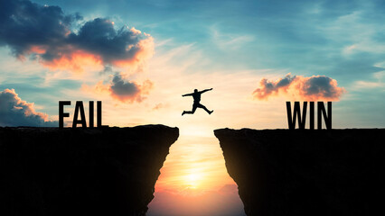 Silhouette of a person jumping from fail to win over a gap between cliffs at sunset, success and...