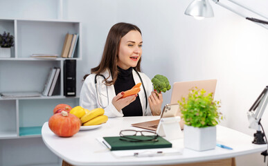 Doctor dietitian in the office with vegetables on table communicates with the patient remotely via...