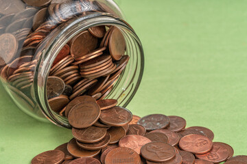 Glass jar filled with US pennies spilling onto a green surface, symbolizing savings, budgeting, and...