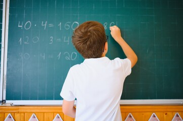 Cute little schoolboy diligent write chalk solve math problem dressed stylish uniform classroom...