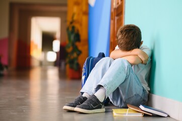 Young boy sitting alone with sad feeling at school. Bullying, discrimination and racism concept with copy space