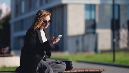 Caucasian woman with curly hair using her mobile phone outdoors. Close-up. Communication technology...