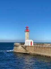 Red-topped tower with white building on a breakwater. Blue sea and clear sky. Coastal landmark and travel. Lighthouse.