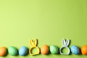 Beautiful decorated Easter eggs and bunny figures on light green background, flat lay. Space for text