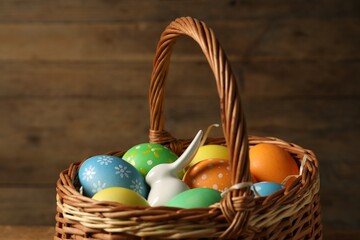 Beautiful decorated Easter eggs and bunny figure in wicker basket, closeup