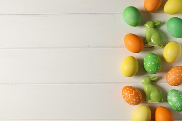 Beautiful decorated Easter eggs and bunny figures on white wooden table, flat lay. Space for text
