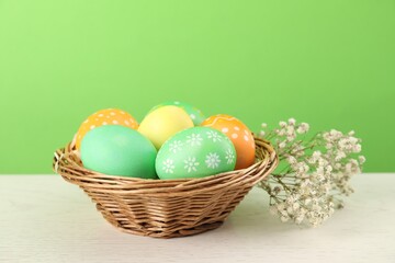 Many decorated Easter eggs in wicker basket and gypsophila flowers on wooden table against light...