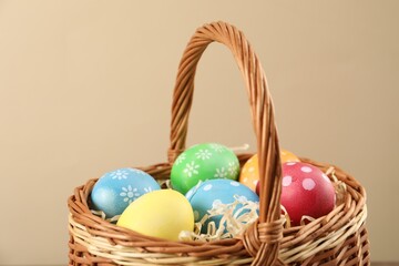 Many decorated Easter eggs in wicker basket on beige background, closeup