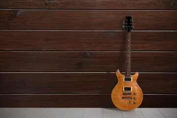 Modern electric guitar on floor near wooden wall. Space for text
