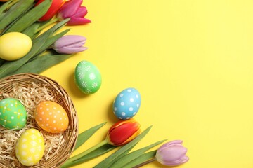 Easter eggs and beautiful tulips on yellow background, flat lay. Space for text